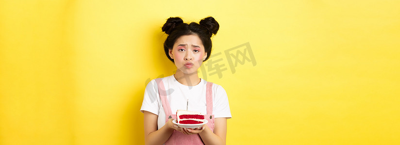 悲伤而孤独的生日女孩皱着眉头，拿着蜡烛的生日蛋糕，许愿，站在黄色背景上