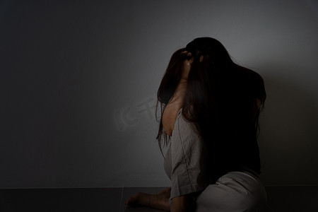 悲伤的女人摄影照片_悲伤的女人抱着她的膝盖，独自坐在黑暗的房间里哭泣。