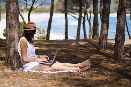 自由职业女性在海边松林中使用笔记本电脑度假工作、智能工作生活方式概念主题和生活选择