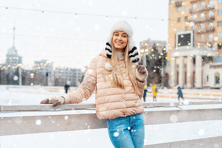 美丽可爱的中年女孩金发保暖冬季夹克针织手套站在溜冰场背景镇广场。