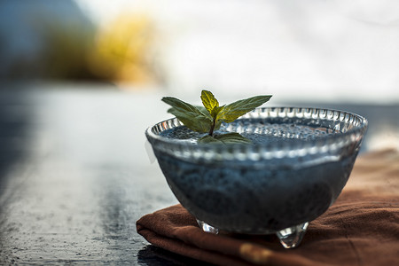 贾斯特罗错觉摄影照片_将浸泡过的 sabja 种子或 falooda 种子或甜罗勒种子放在木质表面棕色餐巾纸上的玻璃碗中，里面有一些薄荷叶。用于许多调味饮料。