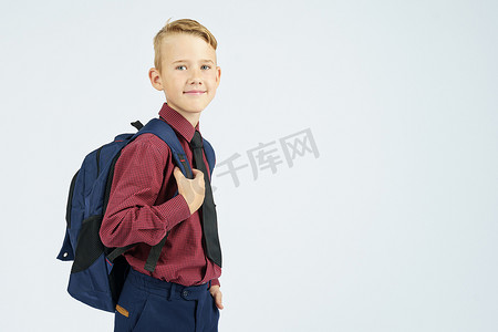 小学生侧身书包摄影照片_一个小学生背着书包，侧身站立，看着镜头。