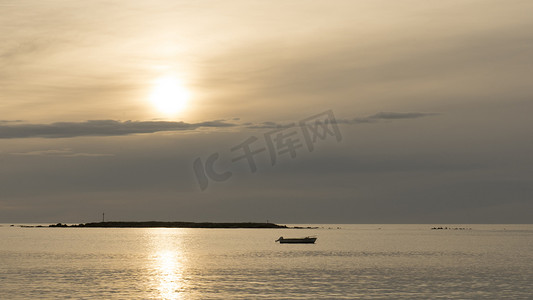 一艘渔船在日出或日落时在背光和多云的天空下停泊在海湾