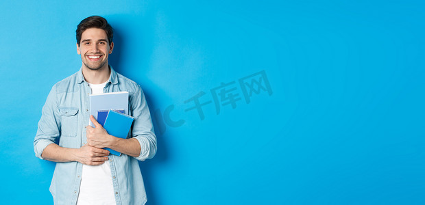 年轻人拿着笔记本和学习材料，笑着开心，站在蓝色背景上