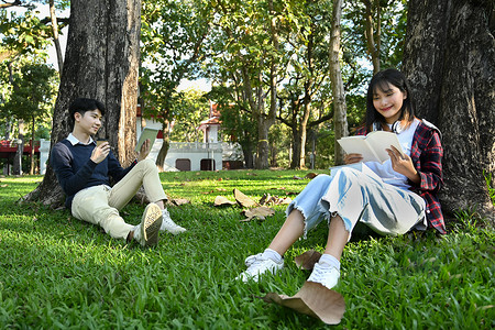 两个微笑的学生读书，在阳光明媚的美好日子在树下准备考试。