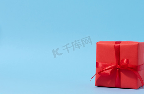 礼盒惊喜摄影照片_蓝色背景上带红丝带的方形红色礼盒，祝贺的背景，惊喜