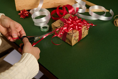 一位女士在包装圣诞礼物时将闪亮的丝带剪成条状以制作漂亮的装饰品的特写镜头