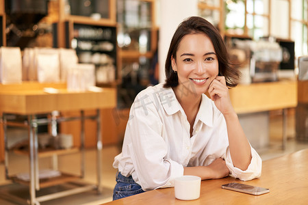 自信的亚洲女性肖像，坐在咖啡馆里，桌上放着智能手机和咖啡。