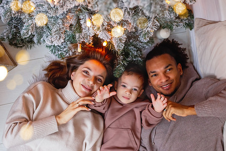 一个幸福的年轻家庭和一个小男孩躺在圣诞树下的针织毯子上。