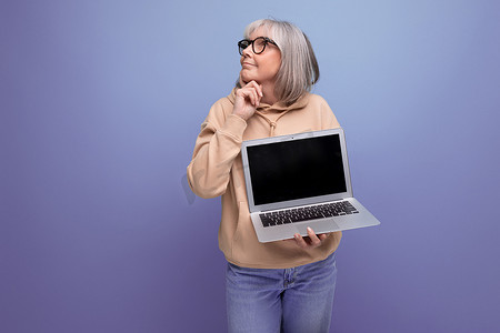 60 多岁头发灰白的成熟女性学习远程职业，手拿笔记本电脑，工作室背景有复制空间