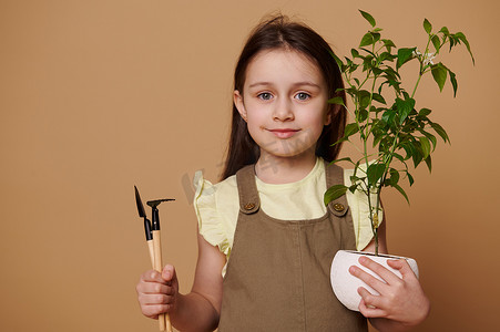 可爱的小女孩，拿着花园铲、耙子和花椒盆栽，对着镜头可爱地笑着。