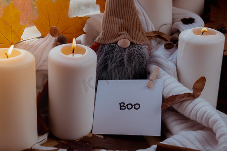 BOO 文本贺卡概念 在窗台上舒适的家中庆祝万圣节秋季假期 Hygge 审美氛围 秋叶侏儒香料和蜡烛在温暖的黄色灯光下的针织白色毛衣上
