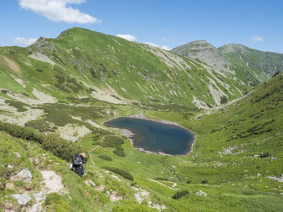 男子徒步前往美丽生动的蓝山湖 Horne Jamnicke pleso，从 Jamnice sedlo 马鞍、Western Tatras 山脉、Rohace 斯洛伐克、夏季阳光明媚的蓝天可以欣赏到绿色山峰
