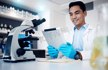科学、平板电脑和显微镜，一个人在实验室工作以进行研究或创新。