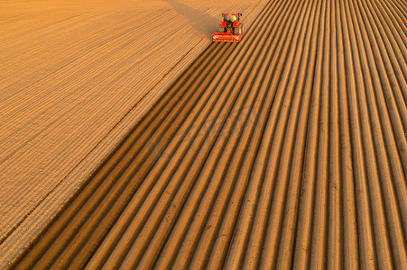 拖拉机在日落时分在农田土壤上犁沟的鸟瞰图。