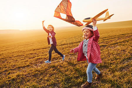 阳光明媚的白天，两个小女孩朋友在田野上玩风筝和玩具飞机