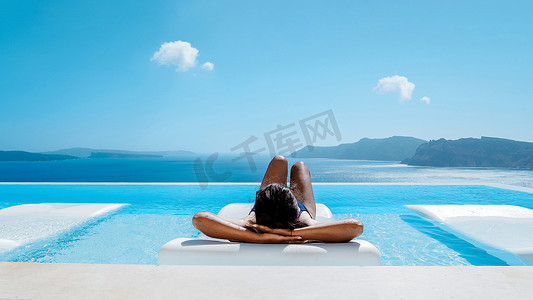 无边泳池中年轻的多文化亚洲女性俯瞰希腊伊亚圣托里尼的海洋