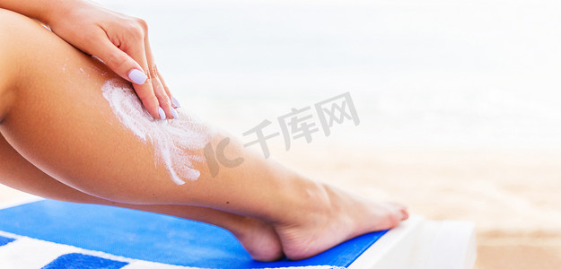 年轻女人正在沙滩上休息，并在腿上涂上防晒霜来保护皮肤