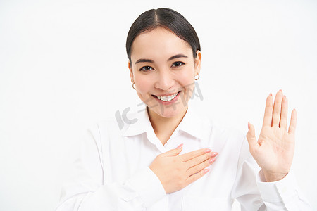 友好的年轻女商人，亚洲女士举起一只手，手掌放在心上，做出承诺，自我介绍，站在白色背景上