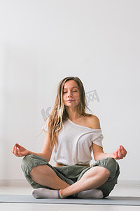 在家练习瑜伽的年轻健康美女坐在瑜伽垫上的莲花姿势上，闭着眼睛微笑放松地冥想 — 正念冥想概念
