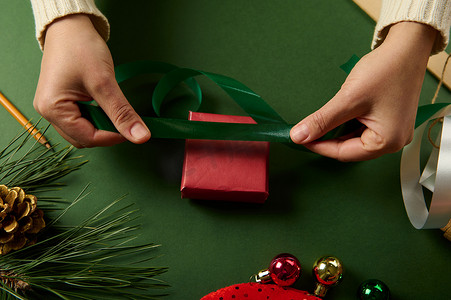 女人的手在绿色背景下包裹圣诞 diy 礼物和礼品盒的顶部视图，带有复制空间。