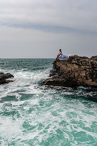 海中石头摄影照片_暴风雨中的女人坐在海中的一块石头上。