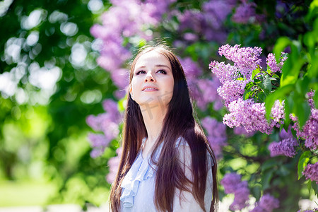 一个快乐的女孩站在开花的丁香花丛旁边，抬头看