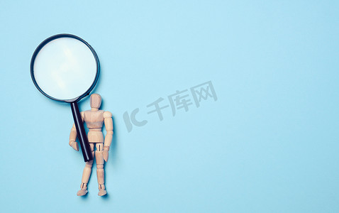 一个木制人体模型在蓝色背景上拿着一个塑料放大镜，这是一个信息搜索、解决问题的概念