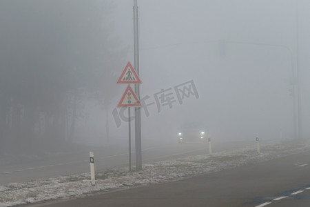 汽车在雾蒙蒙的路上行驶，车头灯或前灯亮着。