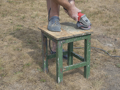 男人用电动磨床、研磨和抛光表面的工具、翻新和抛光旧木制小桌子，在他的花园外面工作。