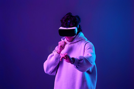 vr虚拟现实摄影照片_戴着 vr 眼镜和运动衫的男人在蓝色背景上玩耍。