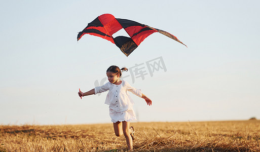 夏天，快乐的小女孩在田野里带着红风筝在户外奔跑