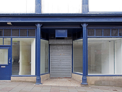 蓝白色城市摄影照片_一家废弃的旧商店的正面漆成蓝白色，店面空荡荡，窗户脏兮兮的，门上的百叶窗紧闭