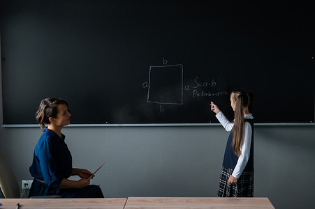 白人小女孩在黑板上回答女老师的问题。