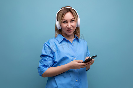 蓝色孤立背景中一位穿着休闲衬衫、戴着白色大耳机听音乐的沉思欧洲女孩的宽屏照片