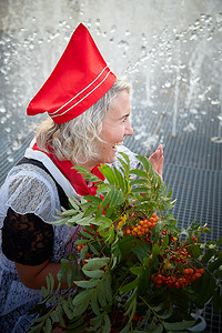 穿着黑色校服、白色围裙和红色领带的女孩靠近喷泉水，手捧一束鲜花。 