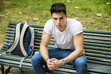严肃地坐在公园长椅上的年轻男学生