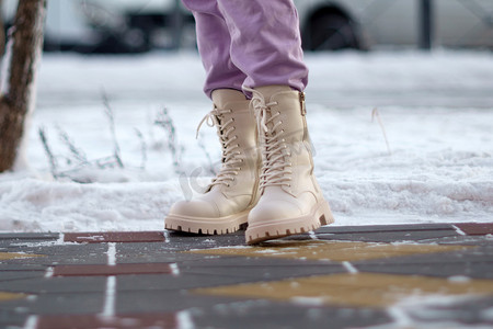 女人走路摄影照片_冬天的一天，白色女靴在雪地上的特写，女人走路。