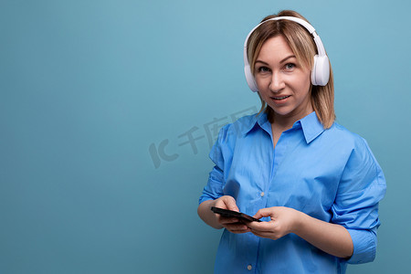 蓝色孤立背景中一位身穿休闲衬衫、戴着白色大耳机听音乐的迷人欧洲女孩的宽屏照片