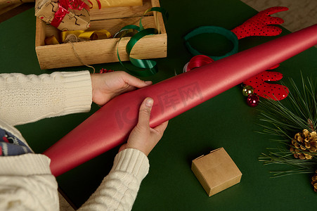 在包装圣诞或新年礼物时，女人的手拿着红色包装纸。