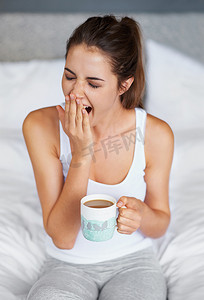 端咖啡的女人摄影照片_还是那么困……一个年轻女人端着咖啡坐在床上打了一个大大的哈欠。