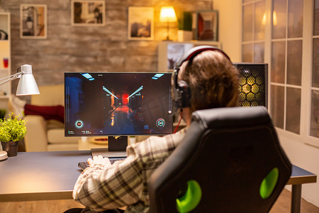 游戏玩家深夜在客厅里用他强大的 PC 电脑玩射击游戏的后视图
