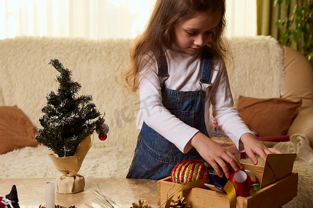 可爱的小女孩站在日记大理石桌旁，木箱里放着圣诞玩具，享受新年准备