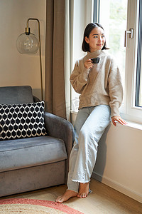 美女坐在家里，望着窗外喝咖啡的垂直照片
