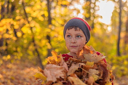 秋天公园里，戴着冬帽的漂亮孩子站着黄色的落叶