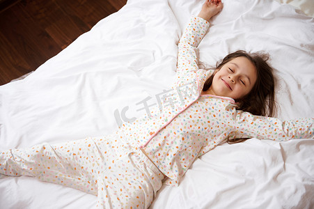 穿着睡衣的可爱小女孩的头像，微笑着躺在一张带矫形床垫的舒适床上