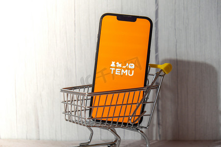 2023年年会摄影照片_波兰格但斯克 — 2023 年 3 月，带有购物车的 iPhone Apple 手机屏幕中的 Temu 应用程序图标。