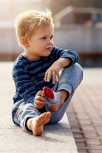 一幅坐在城市喷泉旁的可爱小男孩的画像，孩子脱下袜子，他想在凉水里凉脚