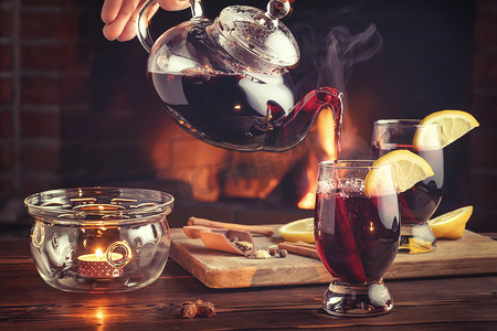 壁炉壁炉摄影照片_在带壁炉的房间里，用茶壶将热红酒倒入玻璃杯中