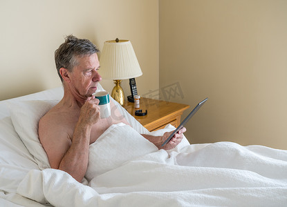 单身白人老人在斜床上阅读数字平板电脑